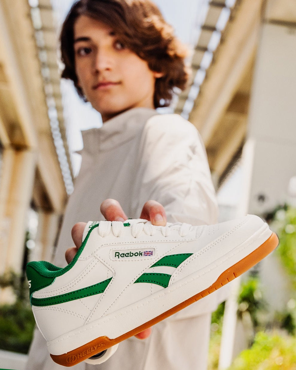 Person holding a Reebok sneaker with a green banner indicating 'Back in Stock' on a blurred outdoor background.