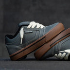 A pair of low-top platform sneakers with a dark gray suede and leather upper, white laces, and a thick brown platform sole, displayed on a dark textured surface.
