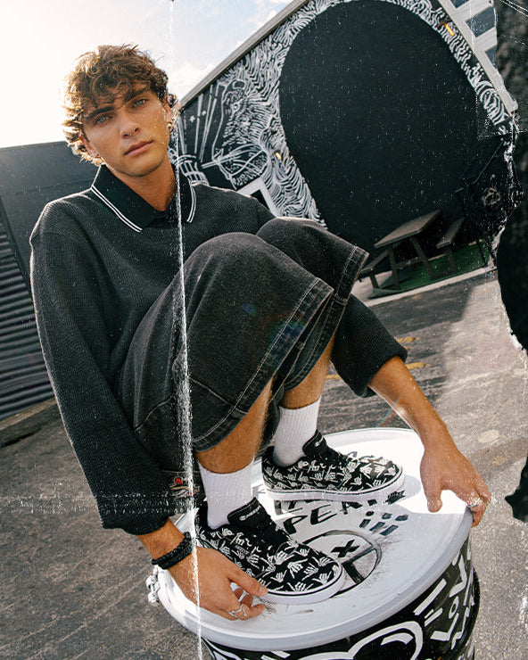 Person wearing black and white sneakers with floral patterns, sitting on a chair.