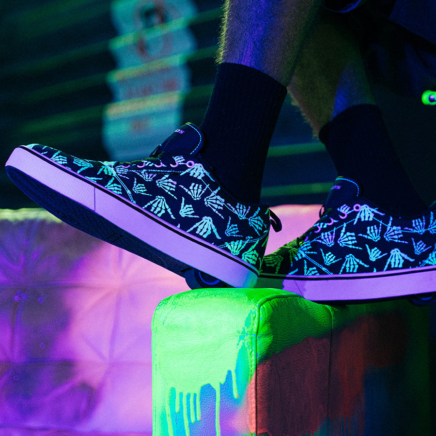 Glowing black shoes with hand designs on a neon green surface.