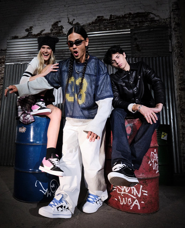 Three people posing on graffiti-covered barrels against a brick wall.