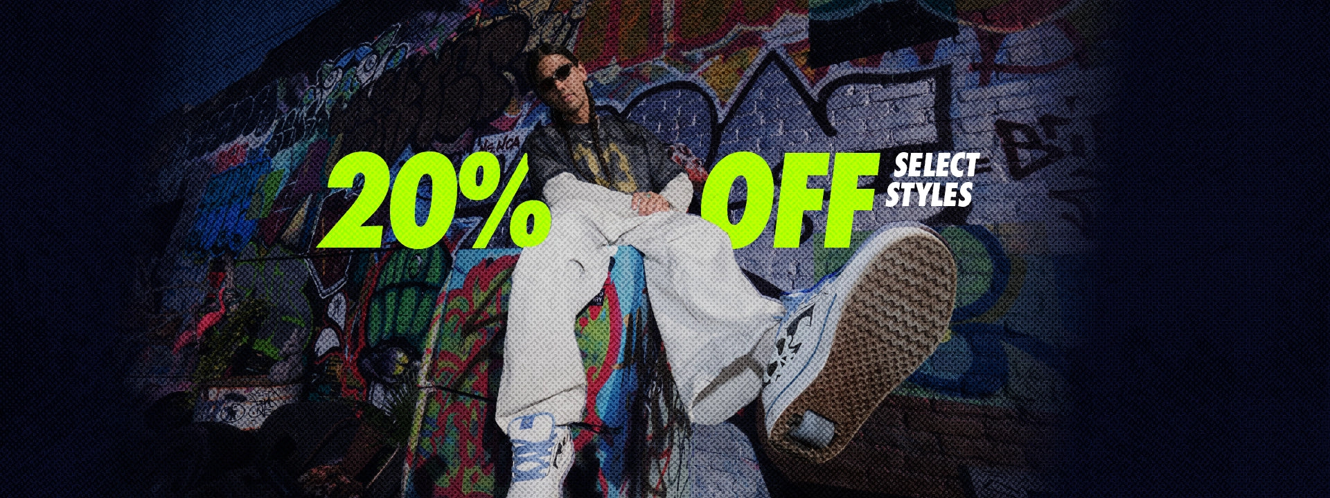 A person wearing white wide-leg pants and a dark jacket sits against a graffiti-covered wall, with one leg raised. Large neon text reads '20% OFF' and 'SELECT STYLES' across the center.