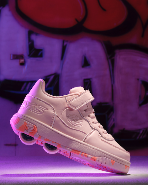 Light pink Heelys logo sneaker with pink wheels on a dark graffiti background